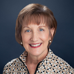 Barb Barhamand smiles into the camera against a dark blue background.